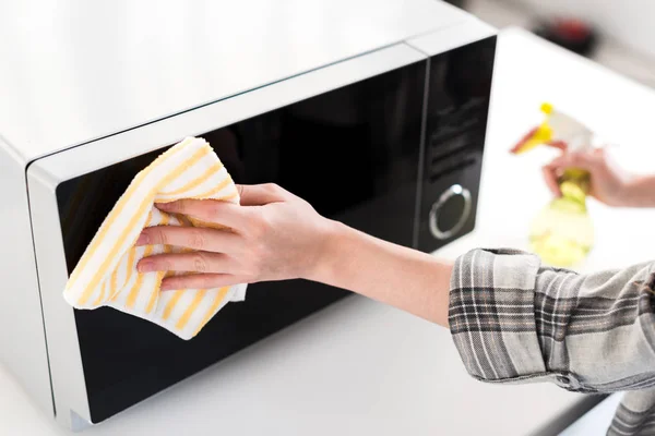 Ausgeschnittene Ansicht einer Frau, die in der Küche Mikrowelle mit Lappen reinigt — Stockfoto