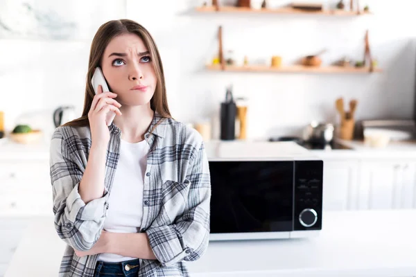Sad woman talking on smartphone near microwave in kitchen — Stock Photo
