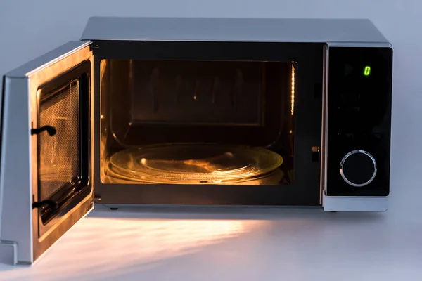 Metal e forno de microondas aberto com luz sobre fundo branco — Fotografia de Stock