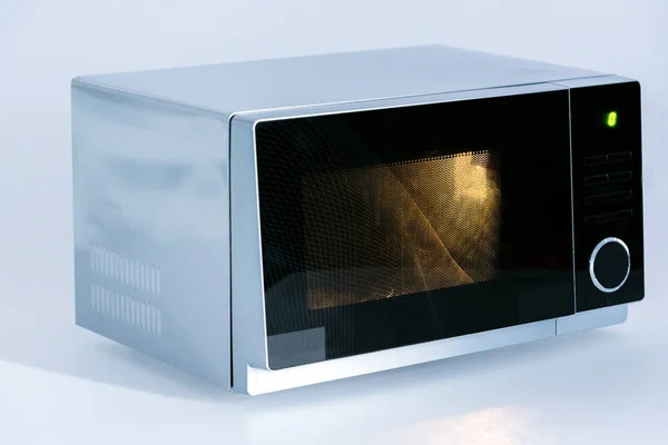 Forno de microondas metálico e elétrico com luz sobre fundo branco — Fotografia de Stock