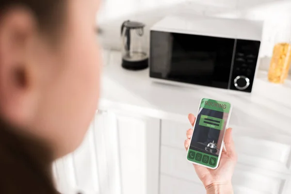 Selective focus of woman holding smartphone with booking app and microwave on background — Stock Photo