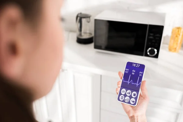 Селективный фокус женщины, держащей смартфон с приложением для здоровья и микроволновой печью на заднем плане — стоковое фото