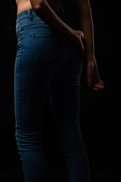 Vue recadrée de jeune fille sexy en jeans posant isolé sur noir — Photo de stock