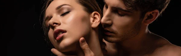 Sexy young couple passionately embracing with closed eyes isolated on black, panoramic shot — Stock Photo