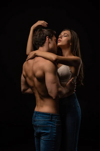 Sexy joven pareja apasionadamente abrazando con los ojos cerrados aislado en negro - foto de stock