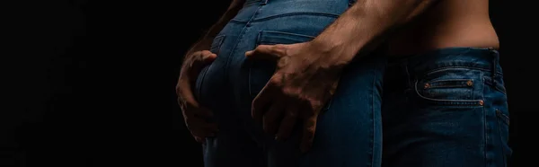 Cropped view of sexy young man touching girlfriend buttocks isolated on black, panoramic shot — Stock Photo