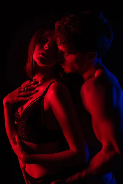 Desvestida sexy joven pareja besándose y abrazándose en rojo luz aislado en negro - foto de stock