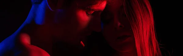 Desvestida sexy joven pareja besándose en rojo luz aislado en negro, tiro panorámico - foto de stock