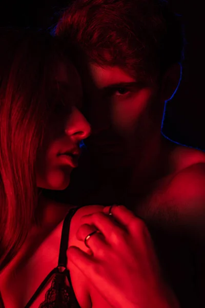 Apasionada desnuda sexy joven pareja abrazando en rojo luz aislado en negro - foto de stock