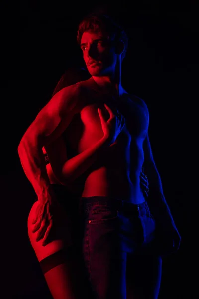 Passionné déshabillé sexy jeune couple toucher l 'autre dans rouge lumière isolé sur noir — Photo de stock