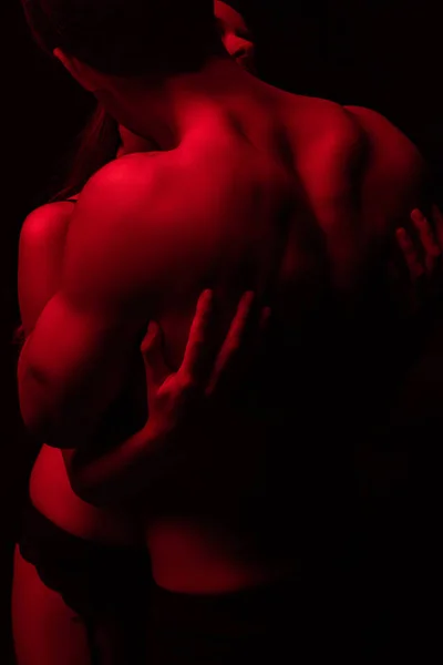 Passionate undressed sexy young couple hugging in red light isolated on black — Stock Photo