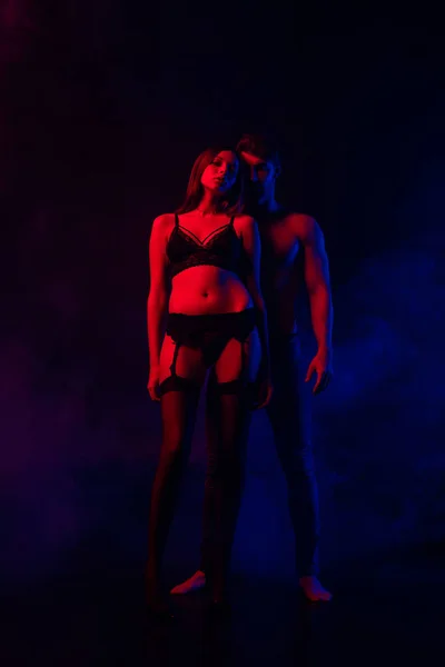 Apaixonado despido sexy jovem casal em vermelho e azul luz no preto fundo — Fotografia de Stock