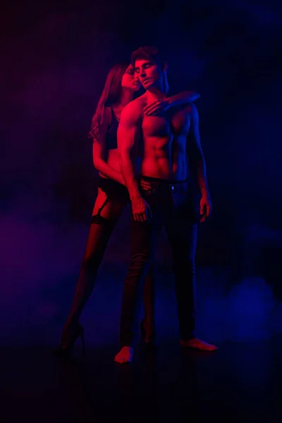 Passionate undressed sexy young couple embracing in red and blue light on black background — Stock Photo