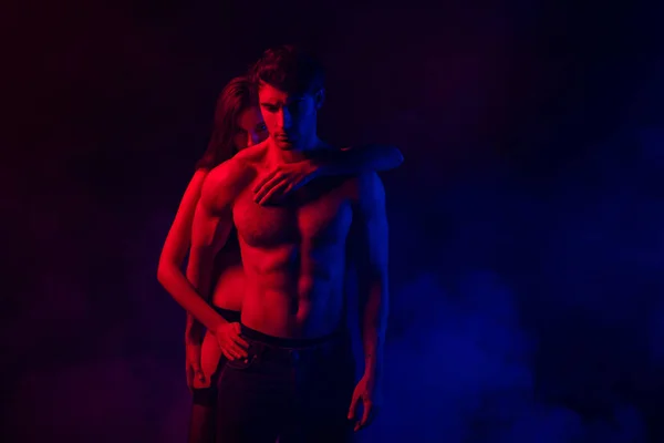 Passionate undressed sexy young couple embracing in red and blue light on black background — Stock Photo
