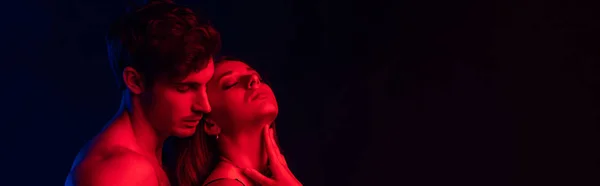 Passionate undressed sexy young couple in red light isolated on black, panoramic shot — Stock Photo