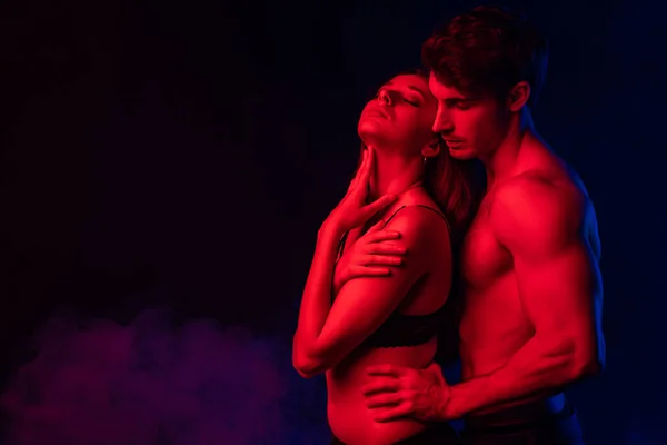 Passionate undressed man touching sexy young woman in red light on black background — Stock Photo
