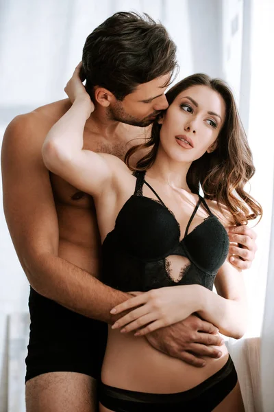 Apasionado hombre besos mejilla de chica en negro ropa interior - foto de stock