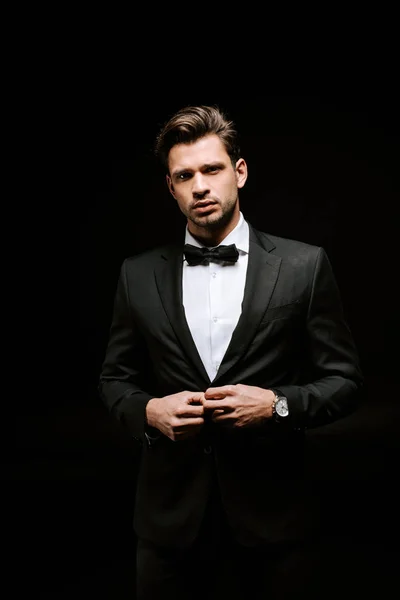 Handsome man in suit touching blazer isolated on black — Stock Photo