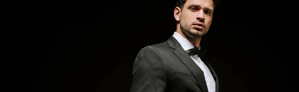 Panoramic shot of elegant man in suit looking at camera isolated on black — Stock Photo