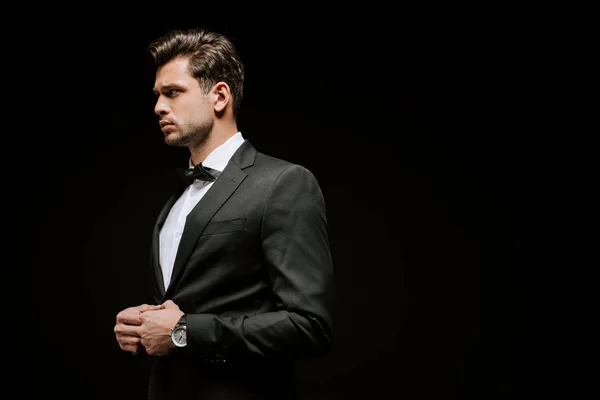 Hombre elegante en traje mirando lejos aislado en negro - foto de stock