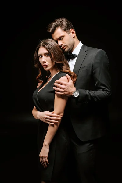 Hombre guapo en traje de pie cerca de mujer elegante aislado en negro - foto de stock