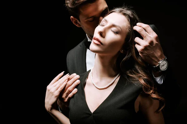 Homme touchant les cheveux de femme séduisante en robe isolé sur noir — Photo de stock