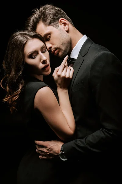 Guapo hombre abrazando joven atractiva mujer aislado en negro - foto de stock
