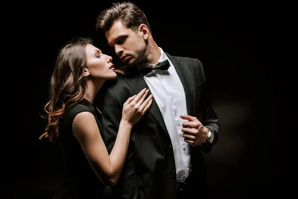 Young attractive woman touching handsome man in suit on black — Stock Photo