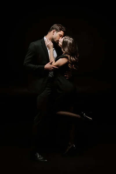 Woman kissing handsome man in suit isolated on black — Stock Photo