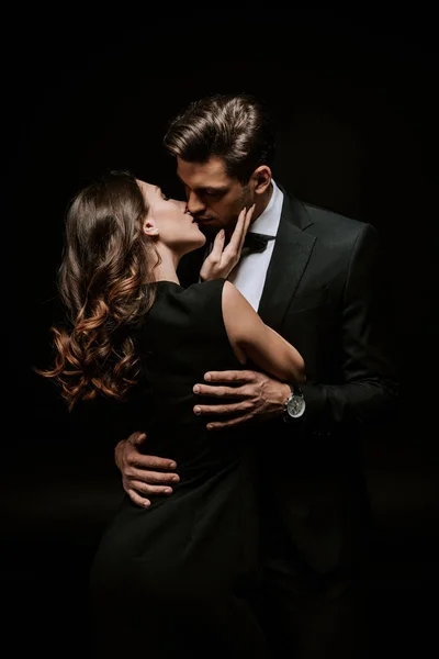 Красива жінка цілує красивого чоловіка в костюмі ізольовано на чорному — стокове фото