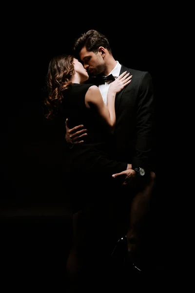 Guapo hombre abrazando sensual mujer en vestido aislado en negro - foto de stock