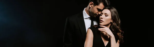 Panoramic shot of sensual man standing with attractive woman in dress on black — Stock Photo