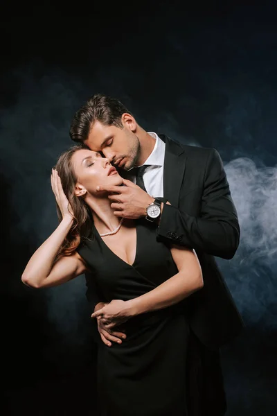 Sensual man touching attractive woman in dress on black with smoke — Stock Photo