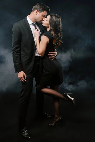 Profile of handsome man in suit hugging woman in dress on black with smoke — Stock Photo