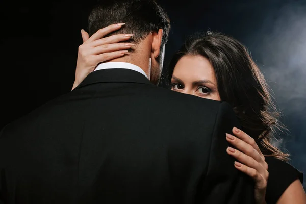 Молода жінка обіймає чоловіка і дивиться на камеру на чорному — стокове фото