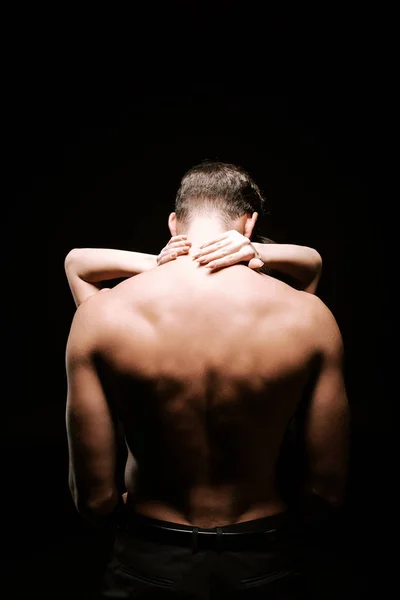 Vista posterior de un hombre sin camisa abrazándose con una mujer aislada en negro - foto de stock