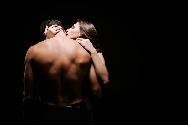 Giovane donna seducente abbracciando fidanzato muscolare isolato su nero — Foto stock