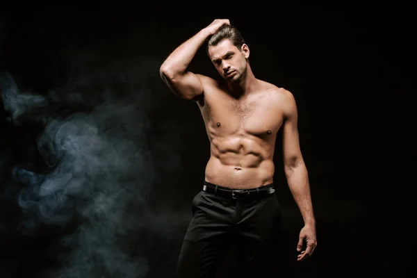 Sexy shirtless man touching hair on black with smoke — Stock Photo