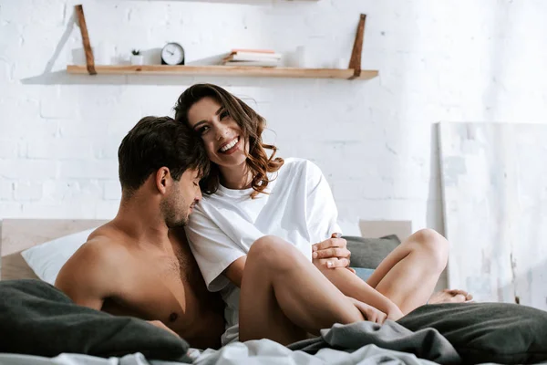 Muscular man smiling near happy girlfriend in bedroom — Stock Photo