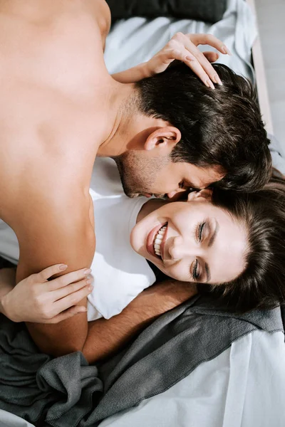Top view of muscular man kissing happy girlfriend in bedroom — Stock Photo
