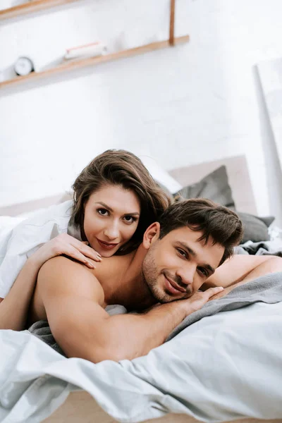 Счастливая молодая женщина лежит в постели с мускулистым парнем — стоковое фото