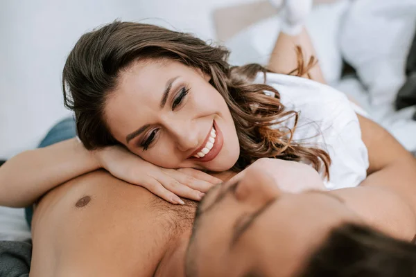 Foco seletivo de feliz jovem deitada na cama com namorado muscular — Fotografia de Stock