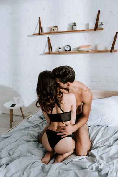 Vista trasera de chica seductora sentada en el hombre sin camisa en el dormitorio - foto de stock
