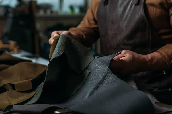 Visão parcial de sapateiro segurando pedaço de couro genuíno na oficina — Fotografia de Stock