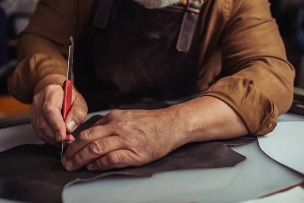 Partial view of cobbler cutting genuine leather with knife — Stock Photo