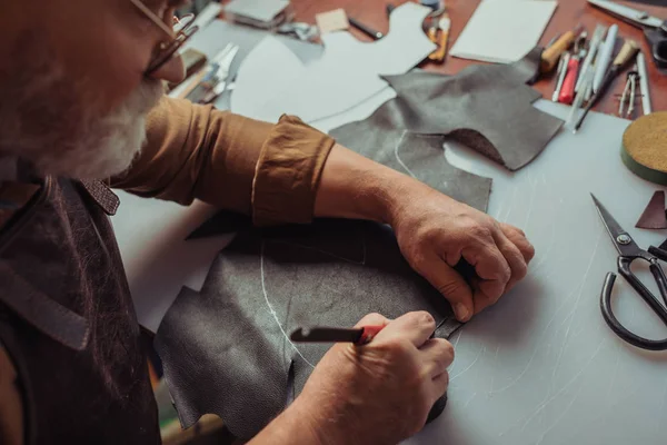 Cropped view of shoemaker cutting genuine leather with knife — Stock Photo