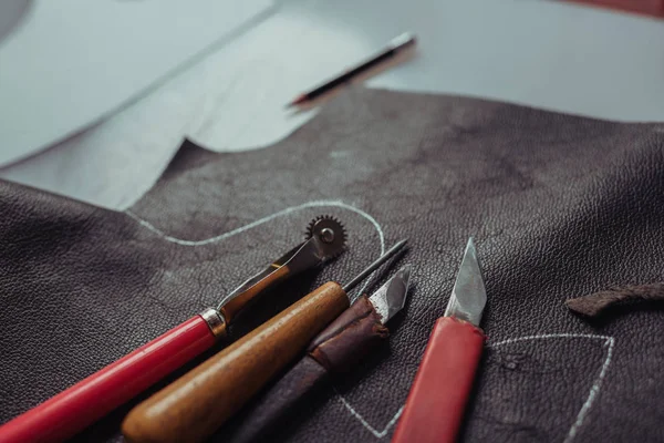 Selective focus of different cutters and tracing wheel on piece of genuine leather in workshop — Stock Photo