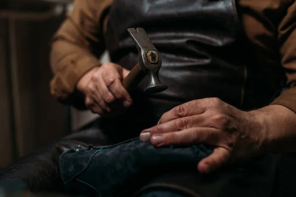 Обрезанный вид сапожника, держащего хаммер во время ремонта обуви в мастерской — стоковое фото