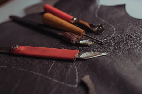 Selective focus of cutters, awl and tracing wheel on genuine leather in workshop — Stock Photo