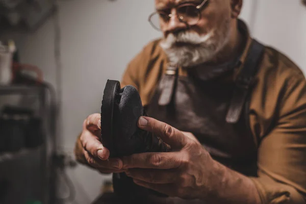 Selective focus of senior cobbler repairing shoe in workshop — Stock Photo